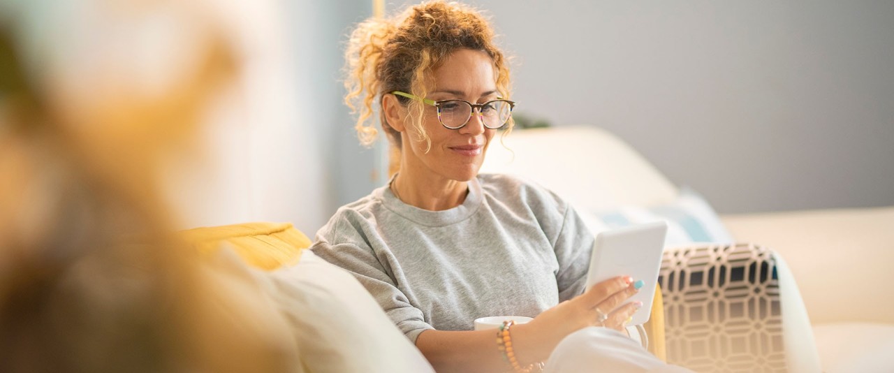Young mature woman smile and enjoy time reading an electronic book on tablet reader device comfortably sitting on the sofa at home in indoor leisure activity alone. Female people have relax indoor Young mature woman smile and enjoy time reading an electronic book on tablet reader device comfortably sitting on the sofa at home in indoor leisure activity alone. Female people have relax indoor